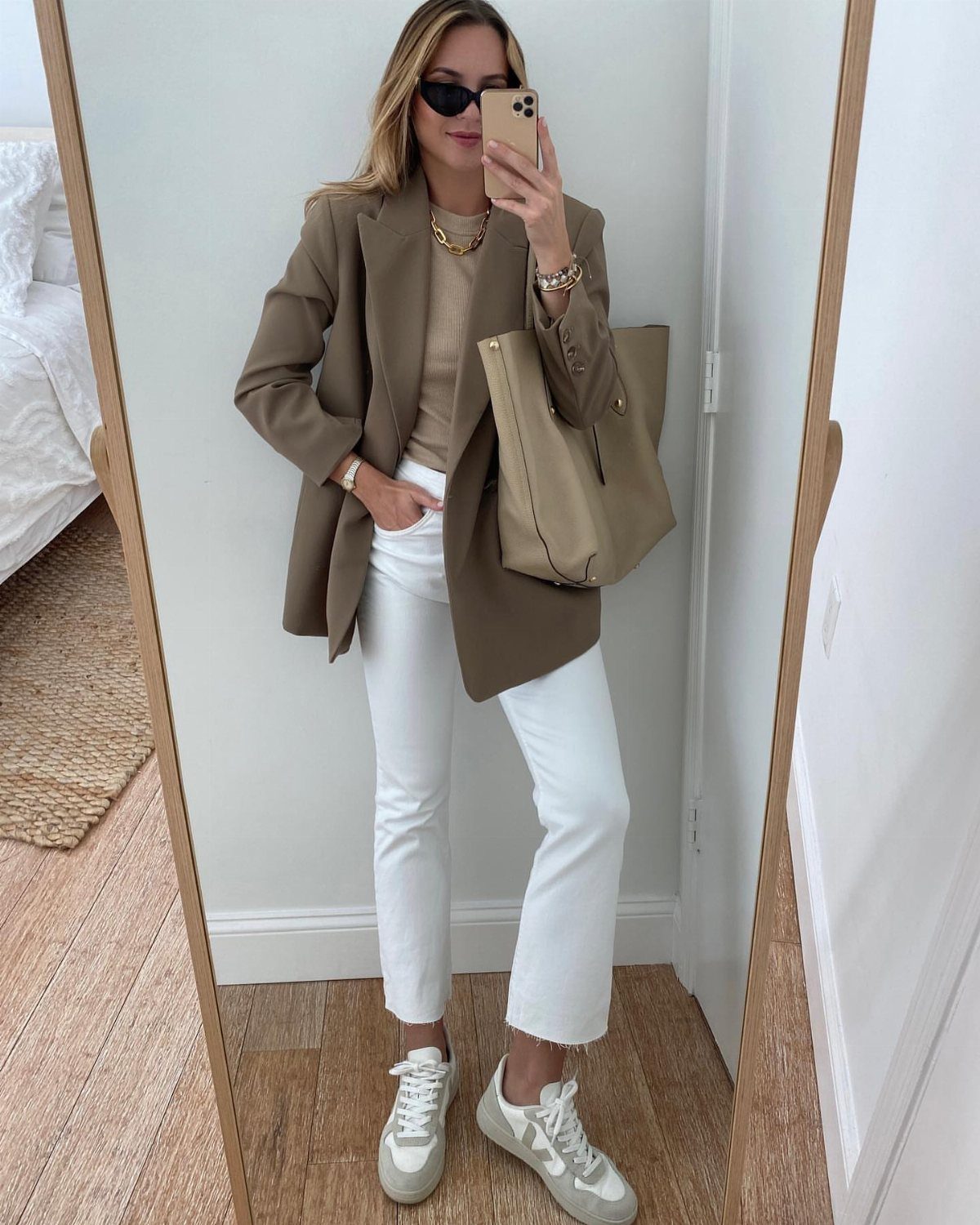 Woman in tan blazer and white pants wearing white Golden Goose sneakers.