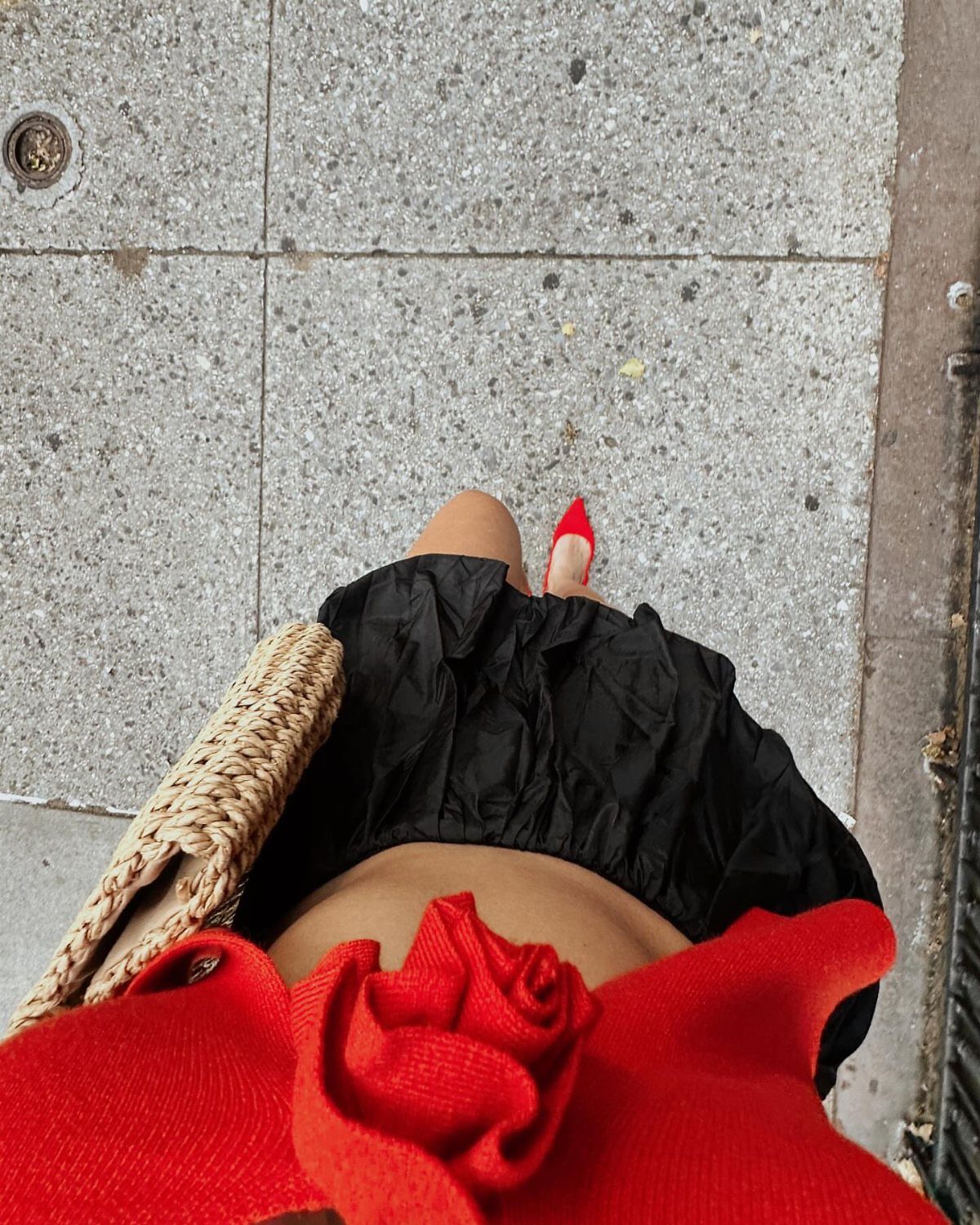 Person wearing a red floral top, black skirt, and red high heels on pavement.