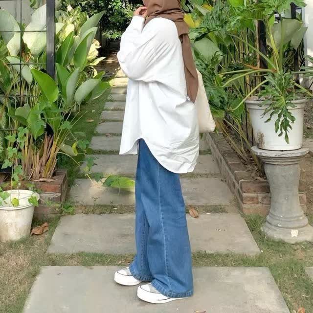 Woman in white shirt and wide-leg blue palazzo jeans standing in a garden.