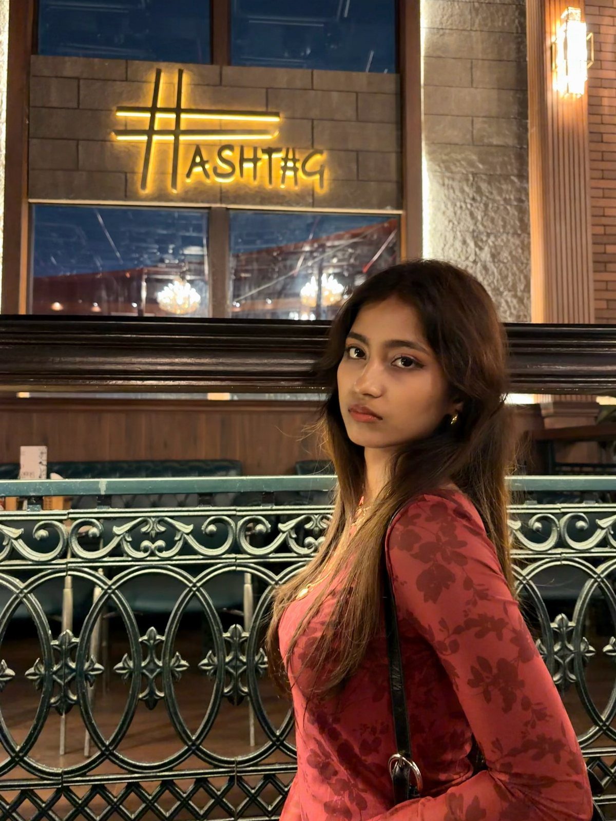 Young woman wearing a wine red floral long-sleeved dress posing outdoors at night.